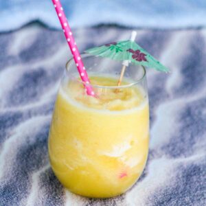 a glass of pineapple ice drink on a sandy beach