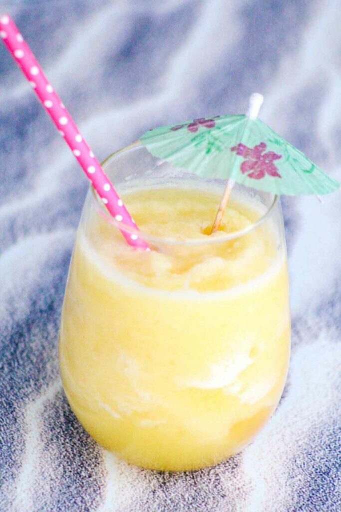 close up of a glass of pineapple ice drink with a paper umbrella and pink paper straw